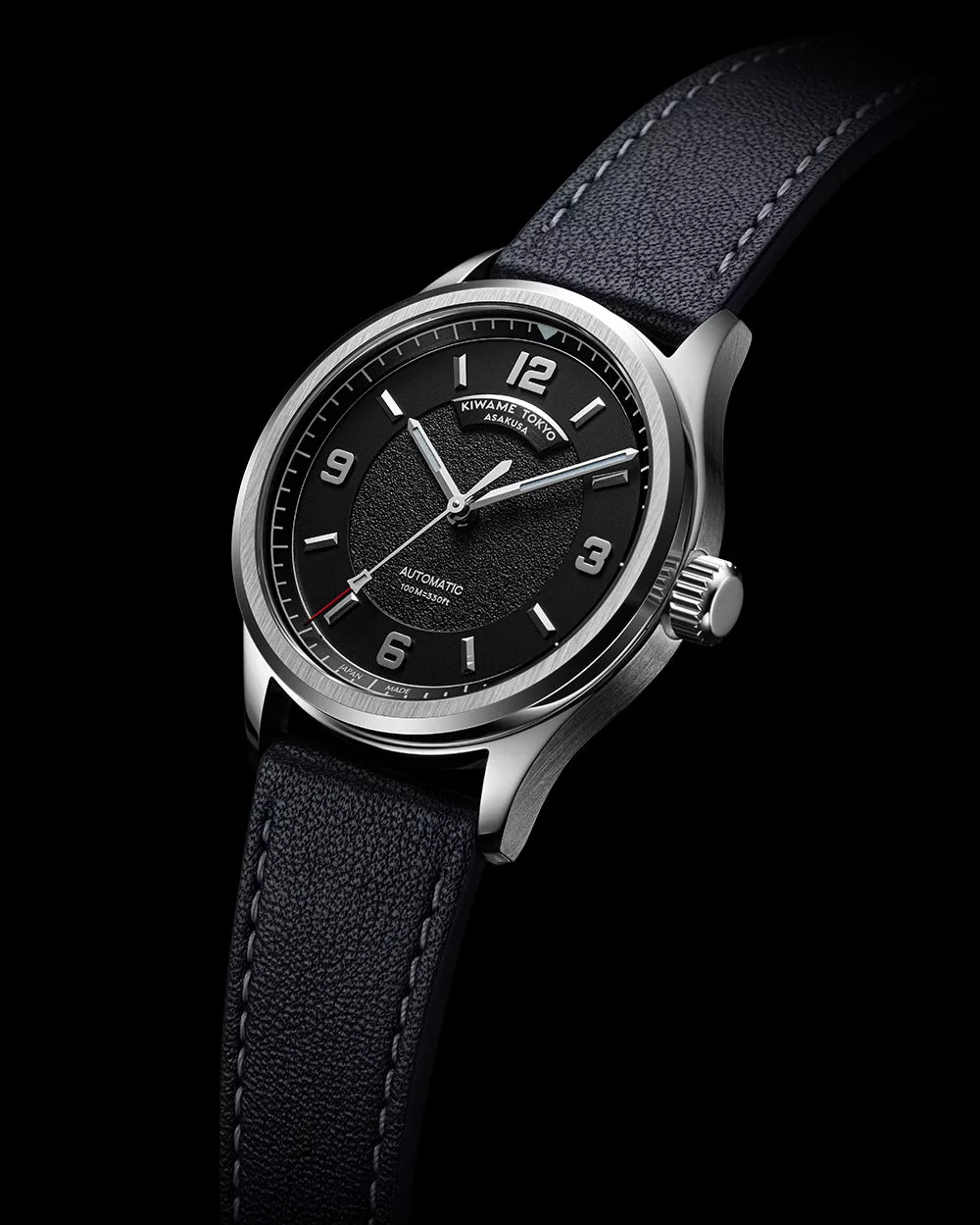 Black dial automatic wristwatch on dark background with brushed stainless steel case and leather strap