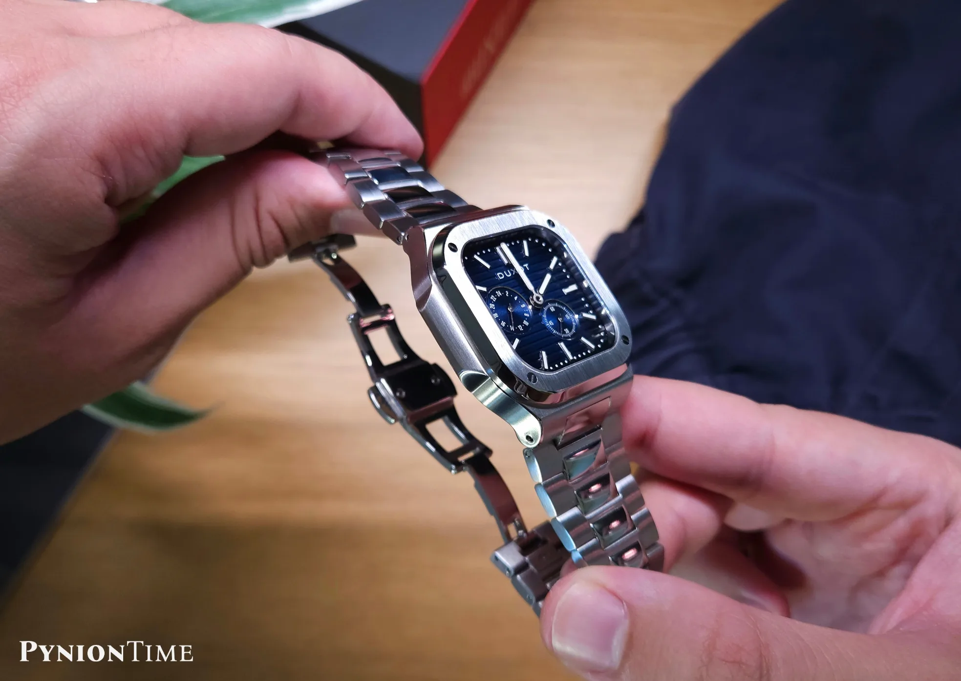 It features a push-button butterfly clasp, shown fully open beside the brushed case side